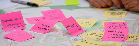Image from a consultation event showing a map with pink and yellow post-it notes on it and a persons hands.