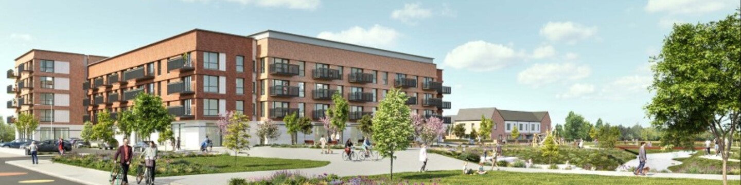 Modern residential development with a red-brick apartment building featuring multiple balconies, set in a landscaped area with trees, shrubs, and flowerbeds. People are walking and cycling along wide paved paths, and a road with large coloured circular patterns runs in the foreground. The sky is bright with scattered clouds