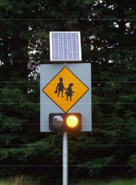 Photo of a school ahead sign with flashing amber signal.